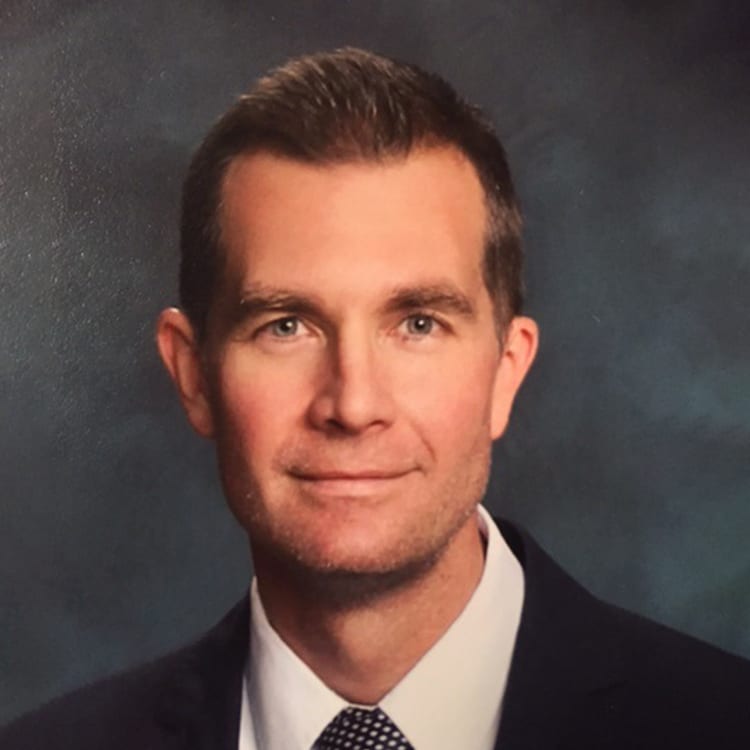 a man wearing a suit and tie smiling at the camera